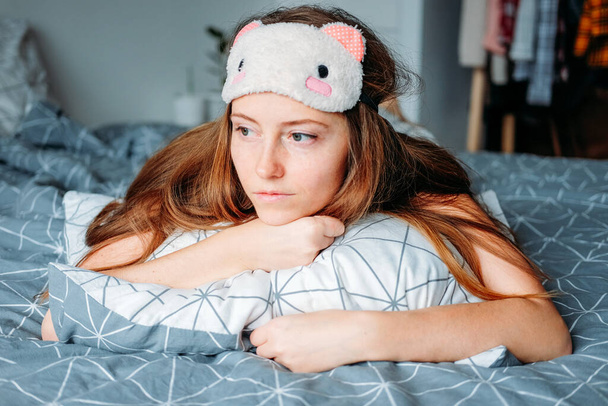 Ärsyyntynyt nuori nainen lepää kotona makaa sängyssä hänen nukkuva naamio ja pyjama - Valokuva, kuva