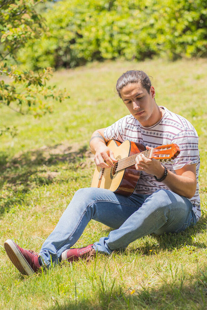 młody człowiek gra na hiszpańskiej gitarze na boisku  - Zdjęcie, obraz