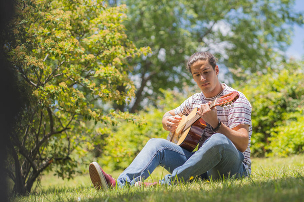 молодий чоловік грає на іспанській гітарі на полі
  - Фото, зображення