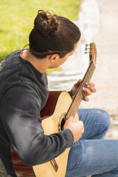 молодий чоловік грає на іспанській гітарі на полі
  - Фото, зображення