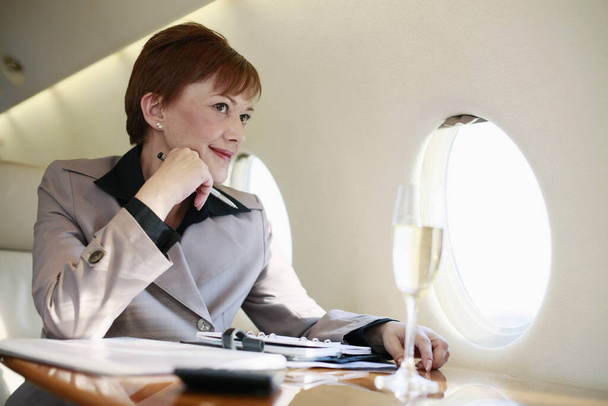 Businesswoman working on private jet while enjoying champagne - Photo, Image