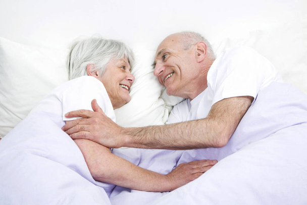 Senior man and woman smiling at each other while sleeping together - Zdjęcie, obraz