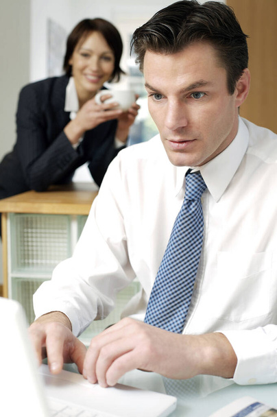 Businessman using laptop with his wife in the background - Foto, Bild