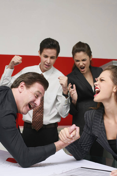 Businessman and businesswoman arm wrestling on table, the others cheering - Photo, image