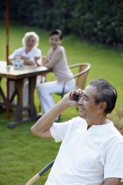 Senior man talking on the phone, senior woman and woman having tea in the background - Photo, Image
