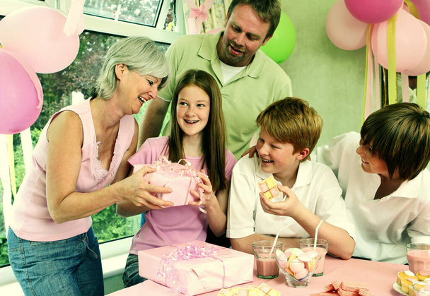 A girl happily receiving her birthday present from her mother while the others watching - Foto, Imagem