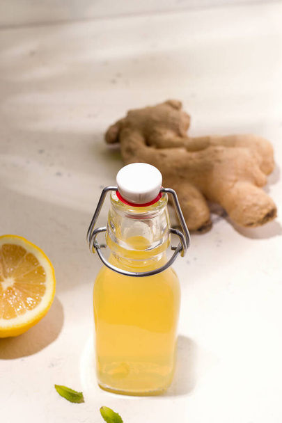 kombucha in een fles naast gember en citroen op een witte achtergrond - Foto, afbeelding