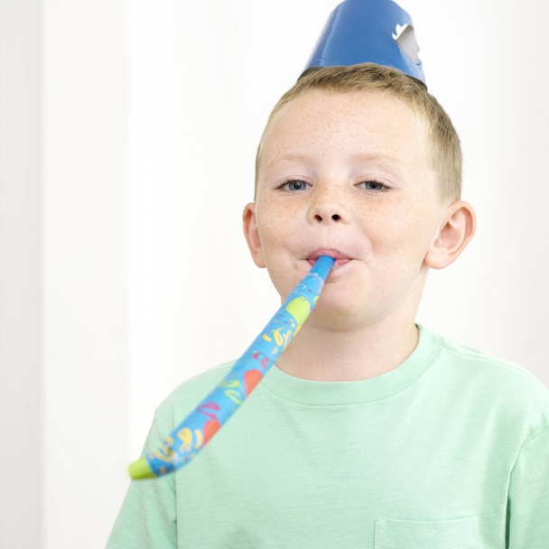 Boy in party hat blowing party horn blower - Foto, Imagem