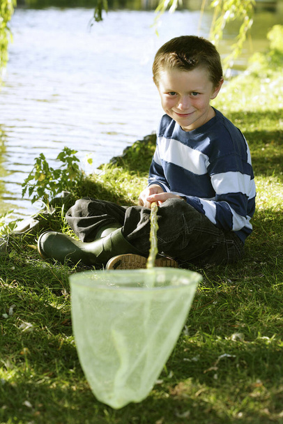 Young boy sitting by the lake side holding fishing net - Photo, Image