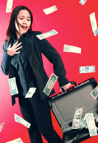 A lady carrying an opened briefcase with all the money flying out from it - 写真・画像