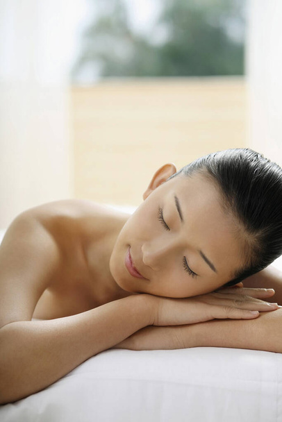 Woman lying forward on massage table with her eyes closed - Foto, Imagem