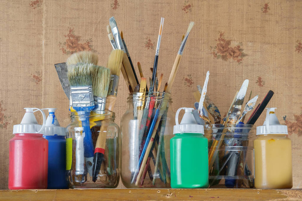 Maaliharjat, maalarit, veitset ja taidelaitteet lasipurkeissa, joissa on akryylimaaleja muoviastioissa - Valokuva, kuva