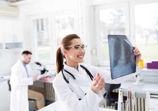 Tevreden vrouwelijke arts met röntgenfoto van de longen en het controleren van de gezondheidstoestand van de patiënt tijdens de pandemie - Foto, afbeelding