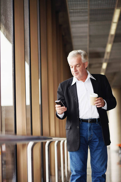 Businessman holding a cup of coffee while text messaging on phone - Photo, Image