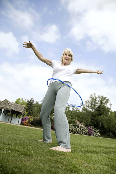 Senior woman playing with plastic hoop in the park - Foto, Imagem