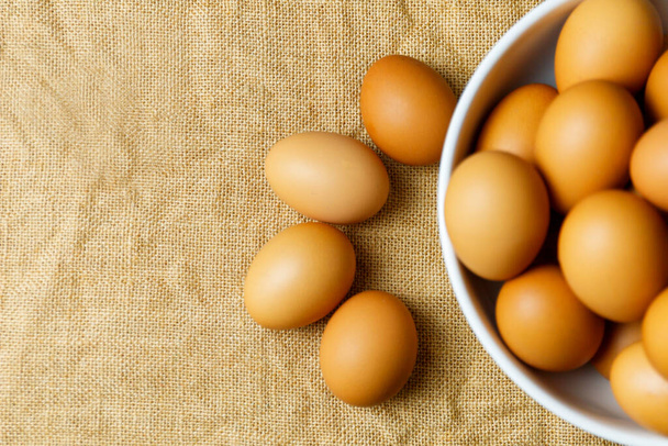 Vista superior de huevos de pollo frescos y borra los huevos de pollo frescos en un tazón blanco sobre un mantel de lino con espacio para copiar. Huevos crudos sin cocer en bowl
. - Foto, Imagen
