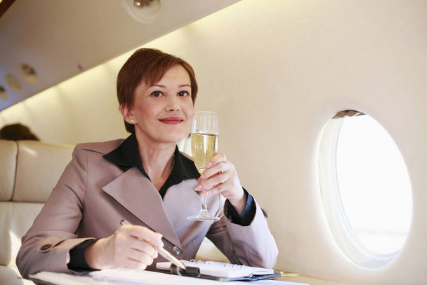 Businesswoman working on private jet while enjoying champagne - Fotó, kép