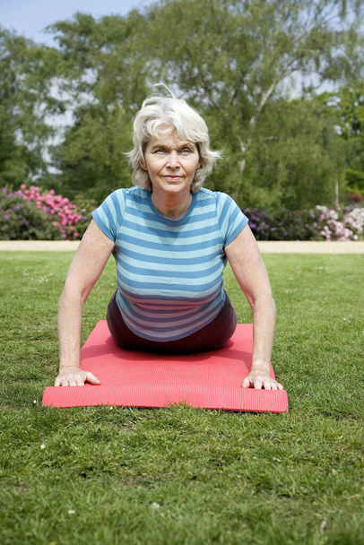 Senior woman practising yoga in the park - Foto, afbeelding