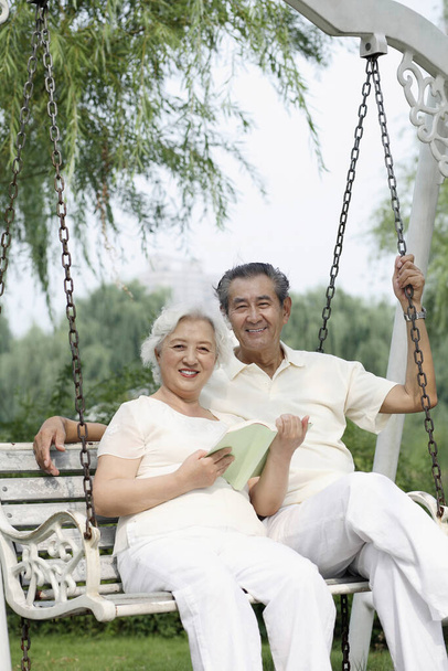 Senior couple smiling at the camera while sitting on a swing - Foto, Imagem