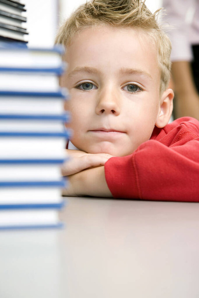 Boy sitting with a stack of books beside him - Zdjęcie, obraz