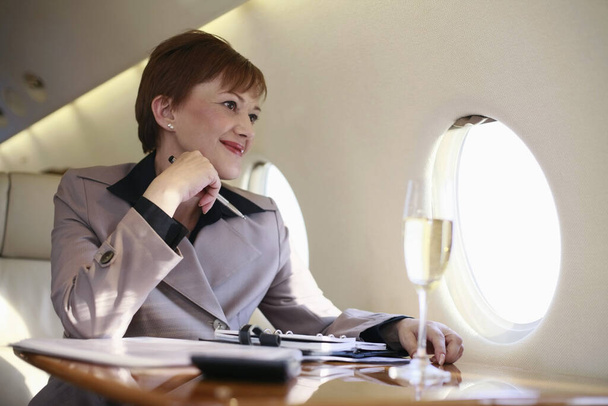 Businesswoman working on private jet while enjoying champagne - Photo, Image