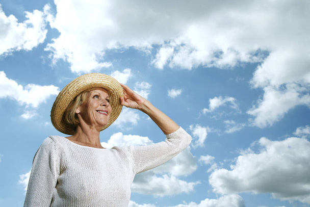 Senior woman holding her hat while looking up - 写真・画像