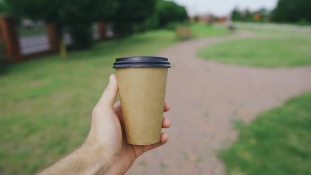 Man carefully carries a hot drink while strolling in the park first-person view - Footage, Video