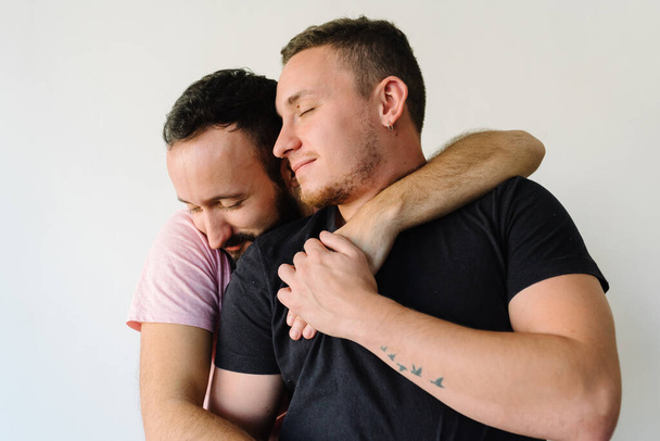 Stock photo of two caucasian homosexual men in their apartment. One of them is hugging the other one from behind. - Photo, Image