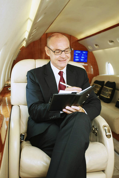Businessman writing in organizer on private jet - Photo, Image
