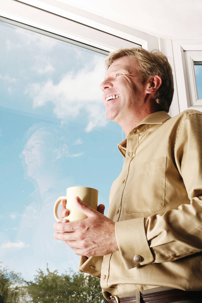 Man holding a cup while looking out of the window - Photo, image