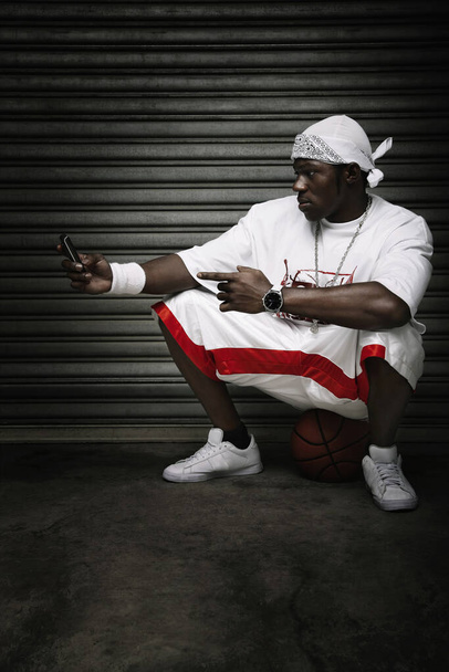 Man sitting on basketball text messaging - Foto, afbeelding