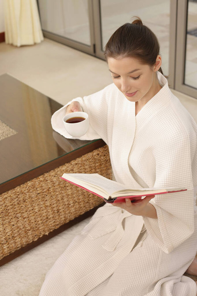 Woman holding a cup of tea while reading book - Foto, Imagem
