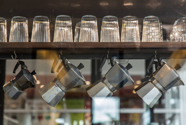 Interior design of coffee shop with glasses and moka pots. Moka pots are hanging on wooden rail. Selective focus - Foto, immagini