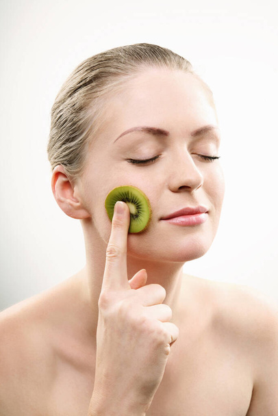 Woman with a sliced kiwi fruit on her cheek - 写真・画像