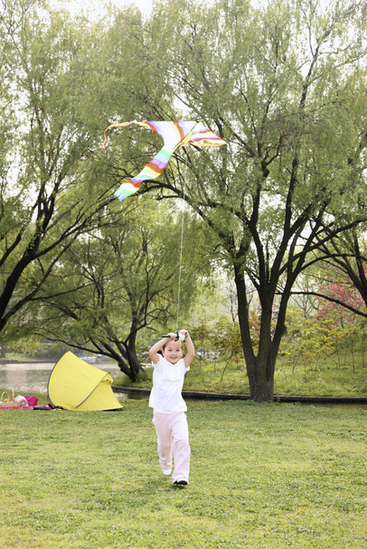 Girl running while flying a kite - Foto, afbeelding