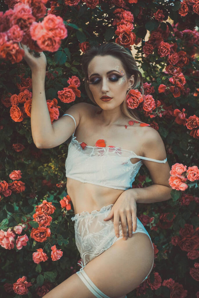 ein junges Mädchen von achtundzwanzig Jahren, in Dessous, auf einem Hintergrund von Textur einer roten Rose. In kreativer künstlerischer Tonung warmer Haut. Natürlicher floraler Hintergrund, Werbung für Unterwäsche - Foto, Bild