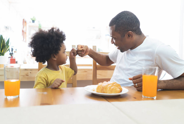 Glücklich lächelnd schlägt die afroamerikanische Familie die Faust beim gemeinsamen Frühstück auf dem Tisch zu Hause. Die Familie genießt das Essen. Glücklicher Vatertag. - Foto, Bild
