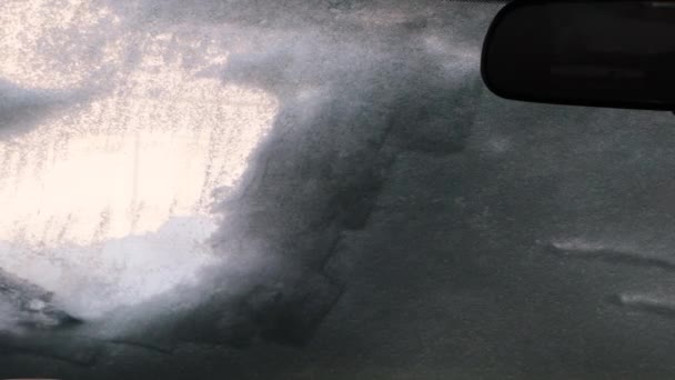 Βλέποντας μέσα από ένα αυτοκίνητο, μια βούρτσα χιονιού καθαρίζει τον πάγο και το χιόνι από το παρμπρίζ. - Πλάνα, βίντεο