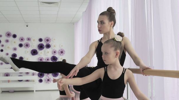 Le ballerine della scuola di danza classica imparano a ballare. Ragazze graziose in abiti neri e rosa ballano il balletto sullo sfondo di una finestra panoramica in studio. - Foto, immagini