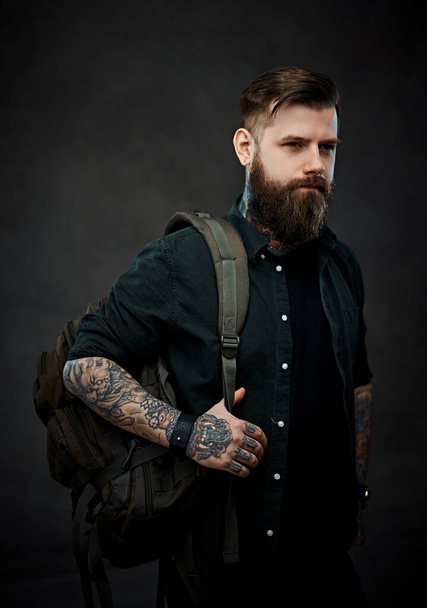 Portrait of a hipster guy with a backpack in a dark studio - Photo, Image