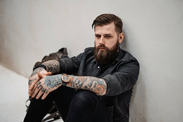 Bearded hipster guy with backpack sitting on a floor in studio - Photo, Image