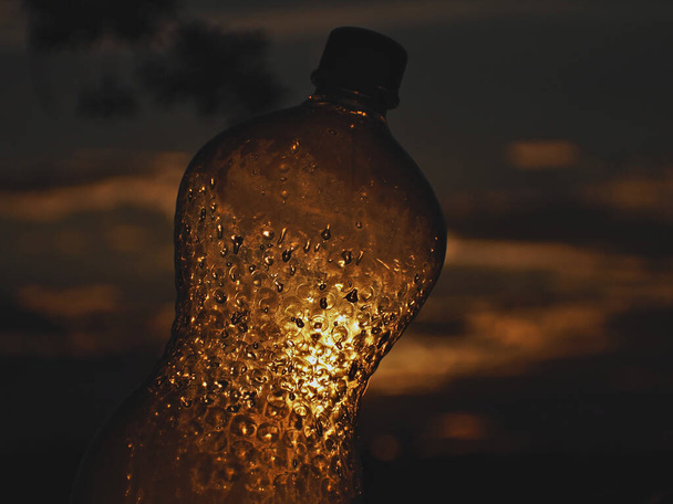 飽和ゴミの中に放置された空のペットボトルを通して日没ができます - 写真・画像