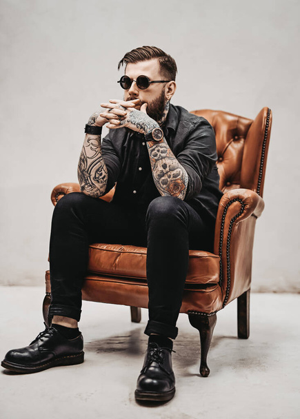 Cool bearded young man sitting on a vintage chair in a studio - Fotografie, Obrázek
