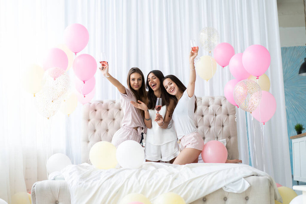 Pajama party. Attractive young smiling women in pajamas drinking champagne while having a slumber party in the bedroom. - Foto, Bild