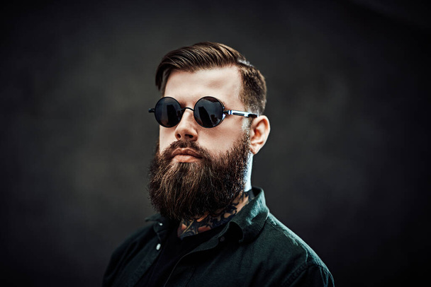 Портрет холодного бородатого чоловіка в сонцезахисних окулярах на темному тлі
 - Фото, зображення