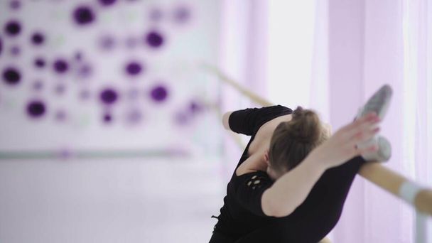 Young thin ballerina in black dress dancing or stretching near a big window. - Fotoğraf, Görsel