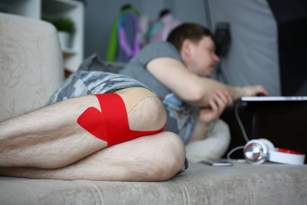 Jeune homme avec jambe blessée couché sur le canapé - Photo, image