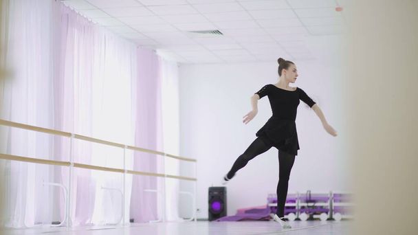 Профессиональная балерина в черном стае танцует в большом тренировочном зале
 - Фото, изображение