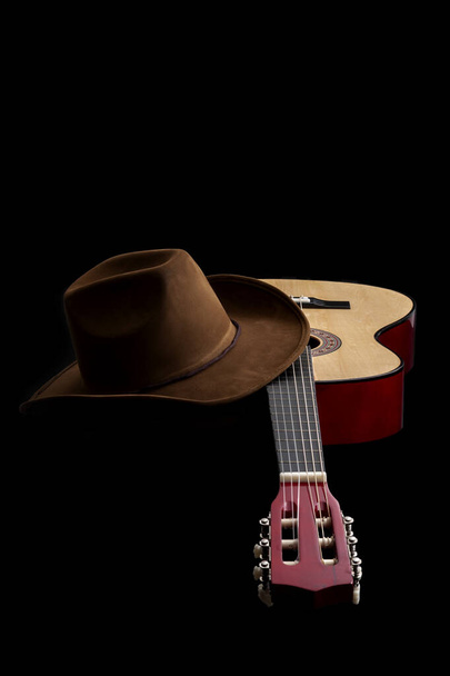 Cultura americana, música folclórica e música country muisc conceito tema com um chapéu de cowboy e uma guitarra acústica isolada em fundo preto com iluminação dramática
 - Foto, Imagem