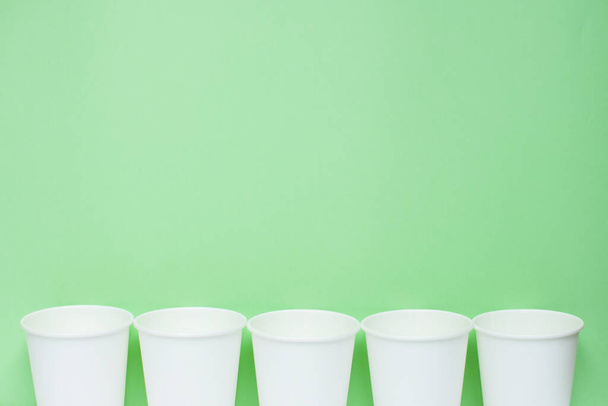 The layout on a green background from white paper disposable cups. Caring for the environment. Recycling garbage. Disposable tableware. - Foto, Imagen